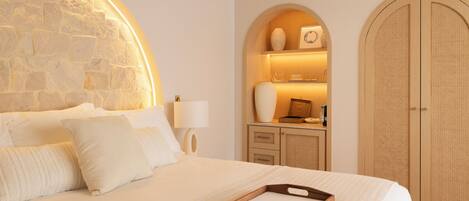 A neatly arranged hotel room with a stone accent wall, a wooden cabinet with a lit shelf, and a large arched wardrobe.