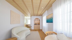 Un salón moderno con un sofá curvo, una mesa de centro de madera, una mesa de comedor con un jarrón y vistas a una cocina y un baño a través de una puerta de cristal.