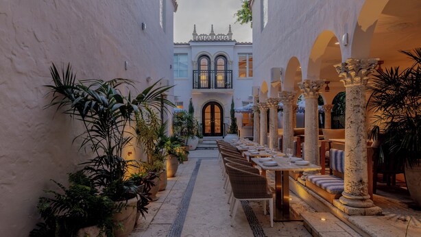 Un patio con zona de comedor, plantas en macetas y columnas.
