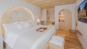 Una habitación de hotel moderna con una cama grande, un cabecero de madera, un pequeño rincón de descanso y vistas al exterior.