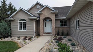 A two-story house with a front entrance, a driveway, and a landscaped garden with various plants and rocks.