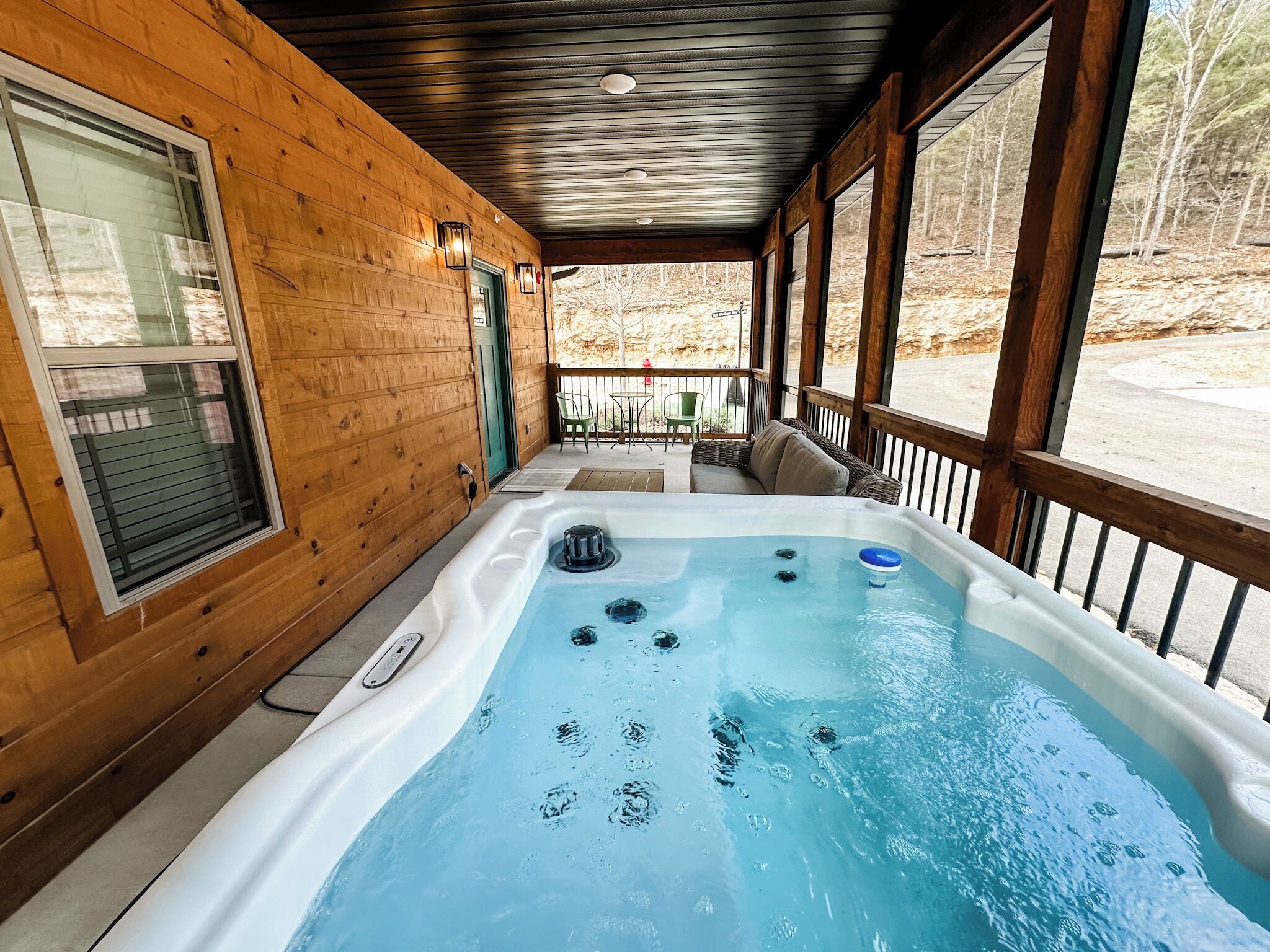 Een houten hut met een hottub, een overdekt terras en uitzicht op het omliggende bos.