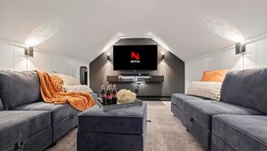 Een gezellige woonkamer met een flatscreen televisie, grijze banken, een bijzettafeltje met lekkernijen en een schaal popcorn.