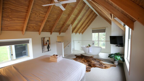 A bedroom with a large bed, a ceiling fan, a mounted TV, and a view of the outdoors.