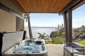 A hot tub with a view of a lake and mountains, wooden ceiling, and outdoor seating.