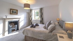 A bedroom with a fireplace, a bed with pillows, a nightstand with a lamp, and a window with curtains.