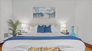 A neatly made bed with a blue blanket, white pillows, and a wooden headboard. There is a painting above the bed and a small plant on the nightstand. - NEW! Southern Retreat w/Pool, BBQ & Game Room (Birmingham)