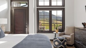 Een slaapkamer met een groot bed, een houten deur en uitzicht op een groen landschap door een raam.