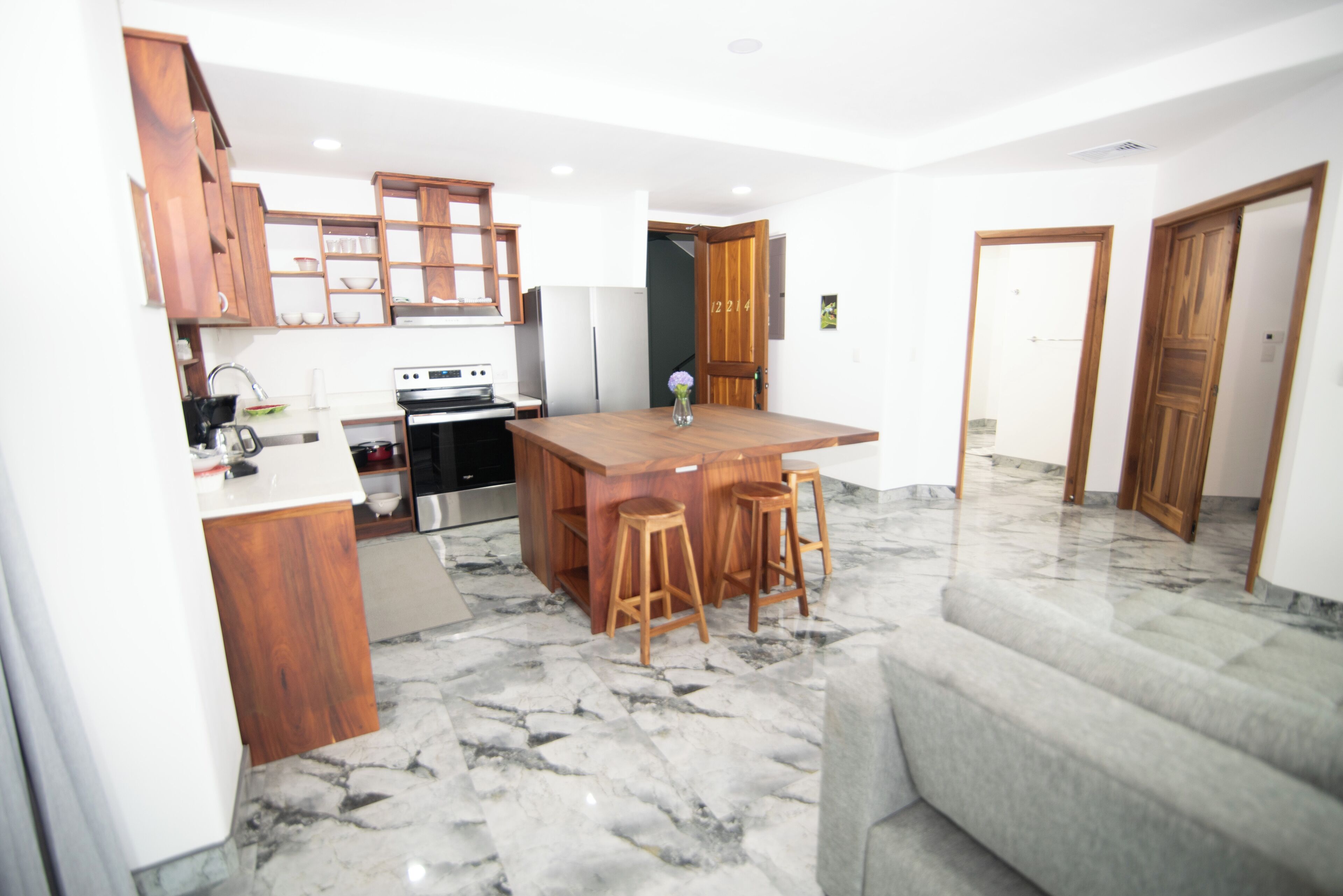 Een moderne keuken met houten kastjes, een marmeren aanrechtblad en een centraal kookeiland met barkrukken.