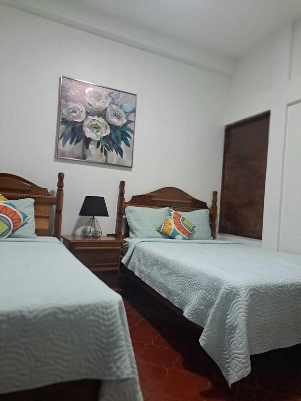 A room with two beds, a painting of flowers on the wall, and a wooden door. - Hotel Casa de Copán (Copán Ruinas)