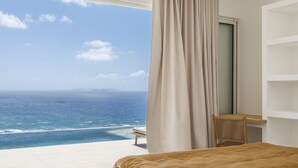 Un dormitorio con un amplio ventanal con vistas al océano, una cama, un escritorio y una silla.