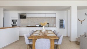 Una cocina moderna con armarios blancos, horno empotrado y comedor con una mesa de madera preparada para seis comensales.