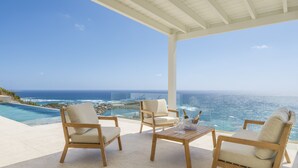 Una terraza con dos sillas de madera y una mesa, con vista a una piscina y al océano.