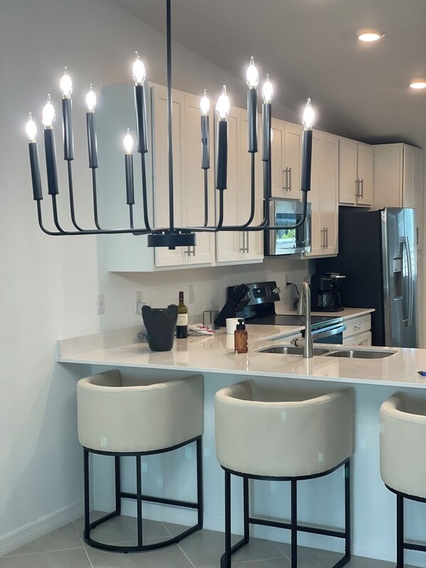 A modern kitchen with white cabinets, a black refrigerator, a built-in oven, and a bar area with stools.