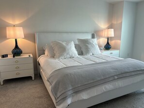 A neatly made bed with white bedding and pillows, flanked by two bedside tables with lamps and clocks.