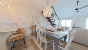 A spacious kitchen with a dining area, white furniture, and a staircase leading to a loft.