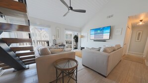 A spacious living area with a modern staircase, two sofas, a round glass table, and a ceiling fan.