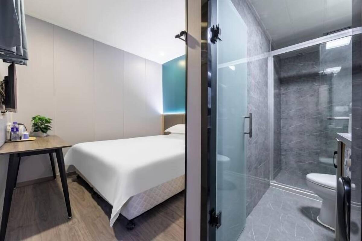 Une chambre d’hôtel avec un lit, un bureau agrémenté d’une plante et un espace douche doté d’une porte en verre.