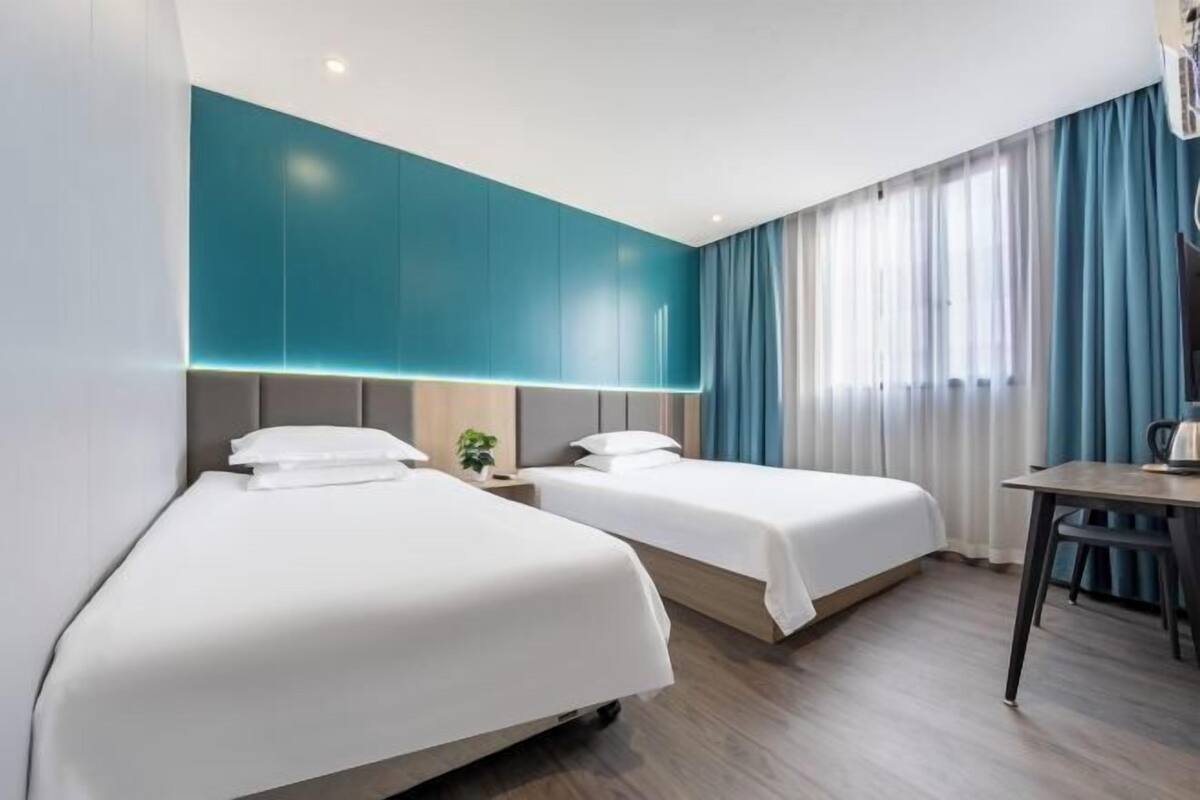 Une chambre d’hôtel avec deux lits, un bureau et une grande fenêtre avec des rideaux.