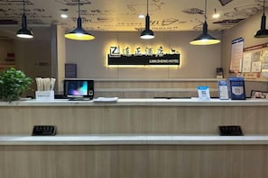 A hotel reception desk with a digital screen, a plant, and a signboard.