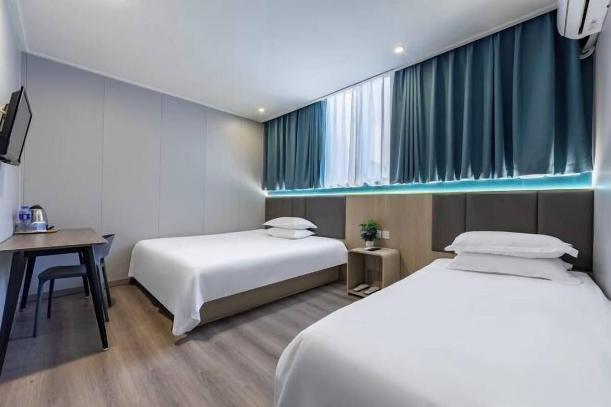 Une chambre d’hôtel avec deux lits, un bureau et une petite table d ’appoint agrémentée d’une plante.