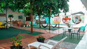 Un vestíbulo de hotel con suelo de madera, césped artificial verde y varias zonas de estar, incluyendo sillones blancos y sillas verdes.