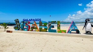 Una playa con letras grandes y coloridas que deletrean 'GALAPAGOS ISABELLA' y una estatua de un pingüino.