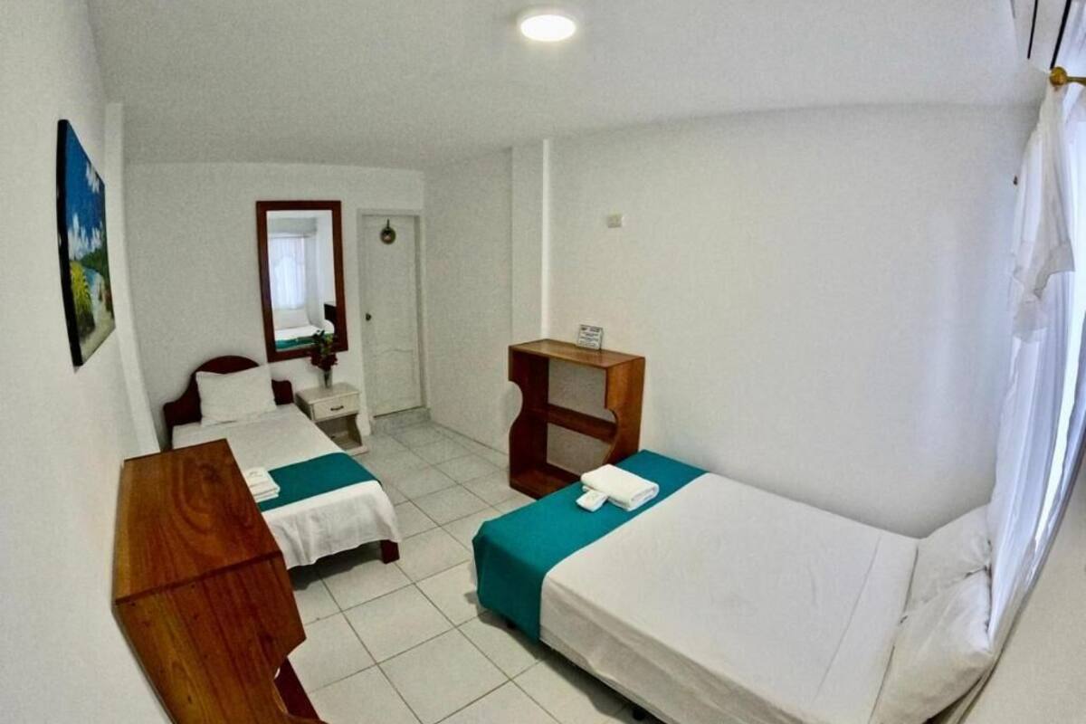 A small, clean room with two beds, a wooden nightstand, a small table, and a mirror.