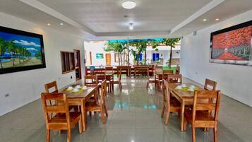 A spacious dining area with multiple wooden tables and chairs, a ceiling with recessed lighting, and artwork on the walls.