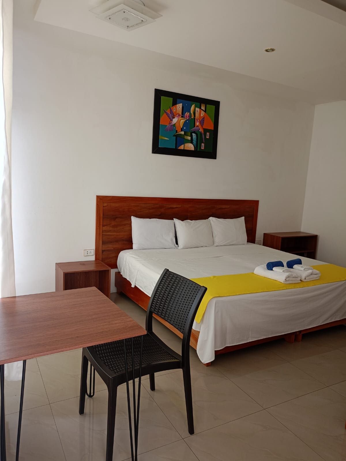 A hotel room with a bed, a desk, a chair, and a painting on the wall.