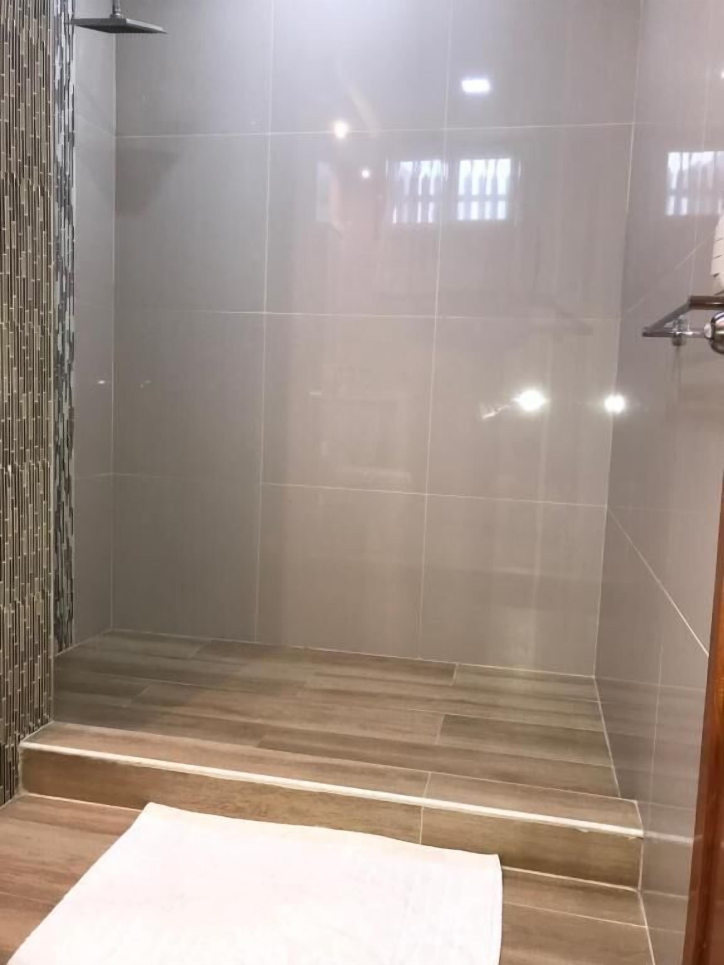 A modern bathroom with a glass shower enclosure, wooden flooring, and a tiled wall.
