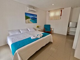 A hotel room with a bed, a chair, a painting, and an air conditioning unit.
