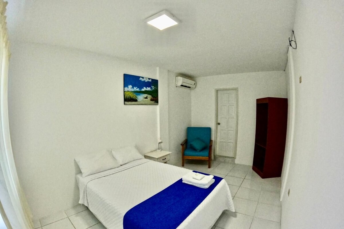 A hotel room with a bed, a chair, a wardrobe, and an air conditioning unit.