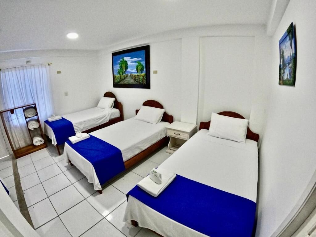 A hotel room with three single beds, white bedding, and blue bedspreads.