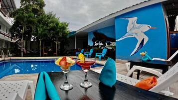 Zona junto a la piscina con sillones de descanso, una mesa con bebidas y un mural de un pájaro.