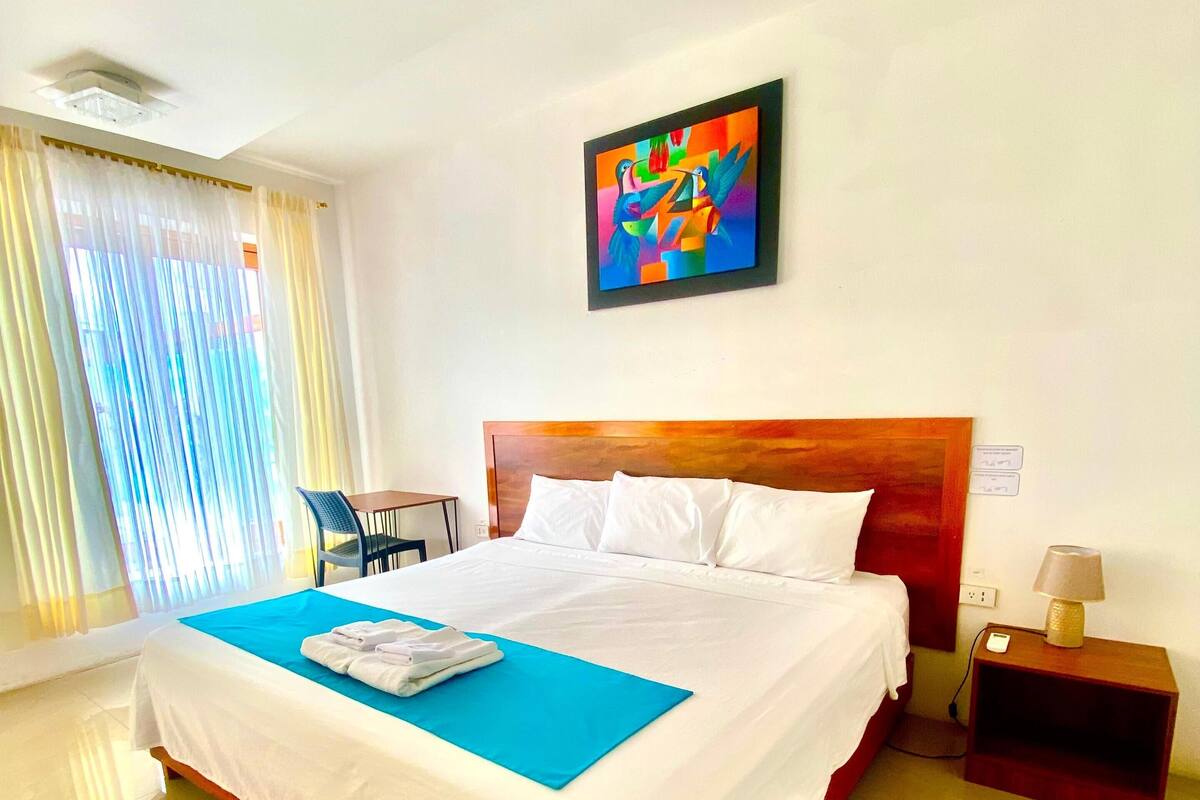 A hotel room with a large bed, a bedside table with a lamp, a chair, and a painting on the wall.