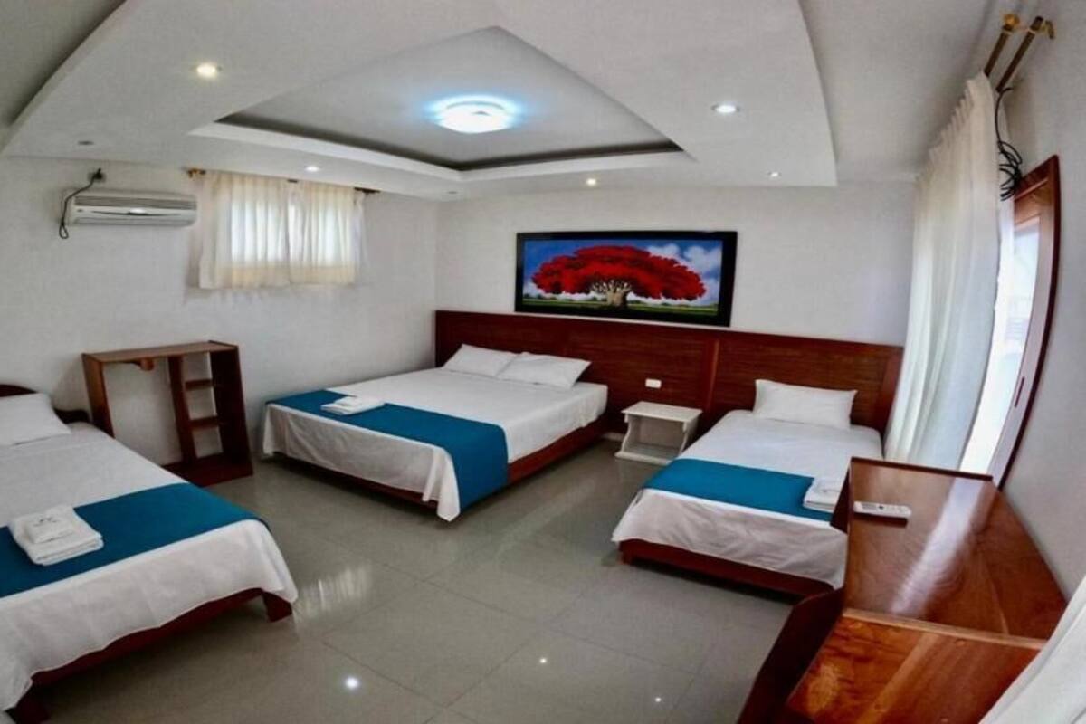 A hotel room with three beds, a wooden headboard, a painting on the wall, and a ceiling light.