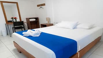A hotel room with a bed, a desk, a chair, a mirror, a wardrobe, and a hanging coat rack.