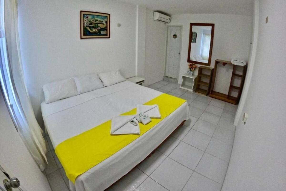 A hotel room with a bed, a small desk, a mirror, and a door.