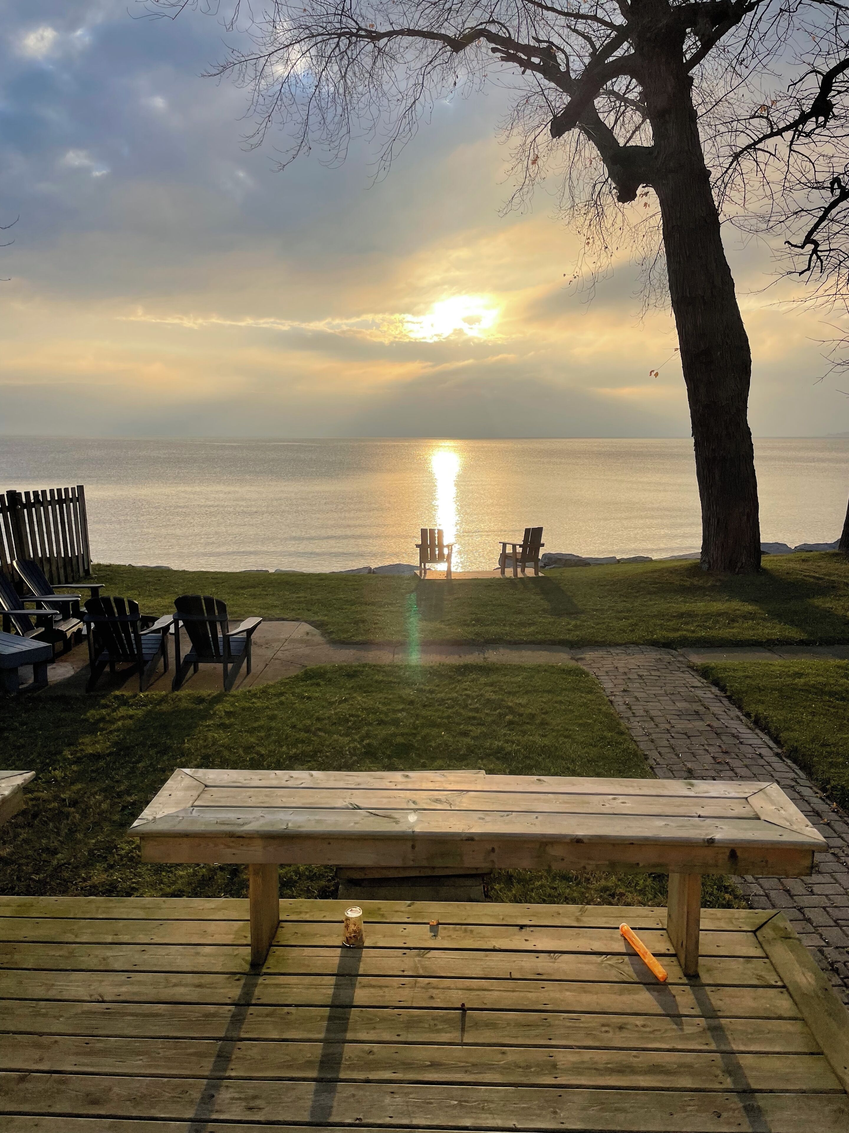 A wooden deck with a bench, two Adirondack chairs, and a small table.
