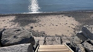 Uma trilha de madeira que leva a uma praia rochosa, com vista clara do oceano.