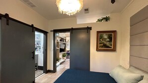 Une chambre avec un lit, une porte donnant sur une salle de bain, un couloir et un espace de vie avec un téléviseur.