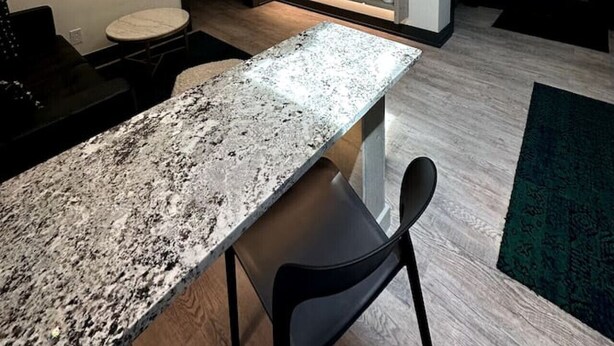 Une cuisine moderne avec un plan de travail en granit, des chaises noires et un lustre.