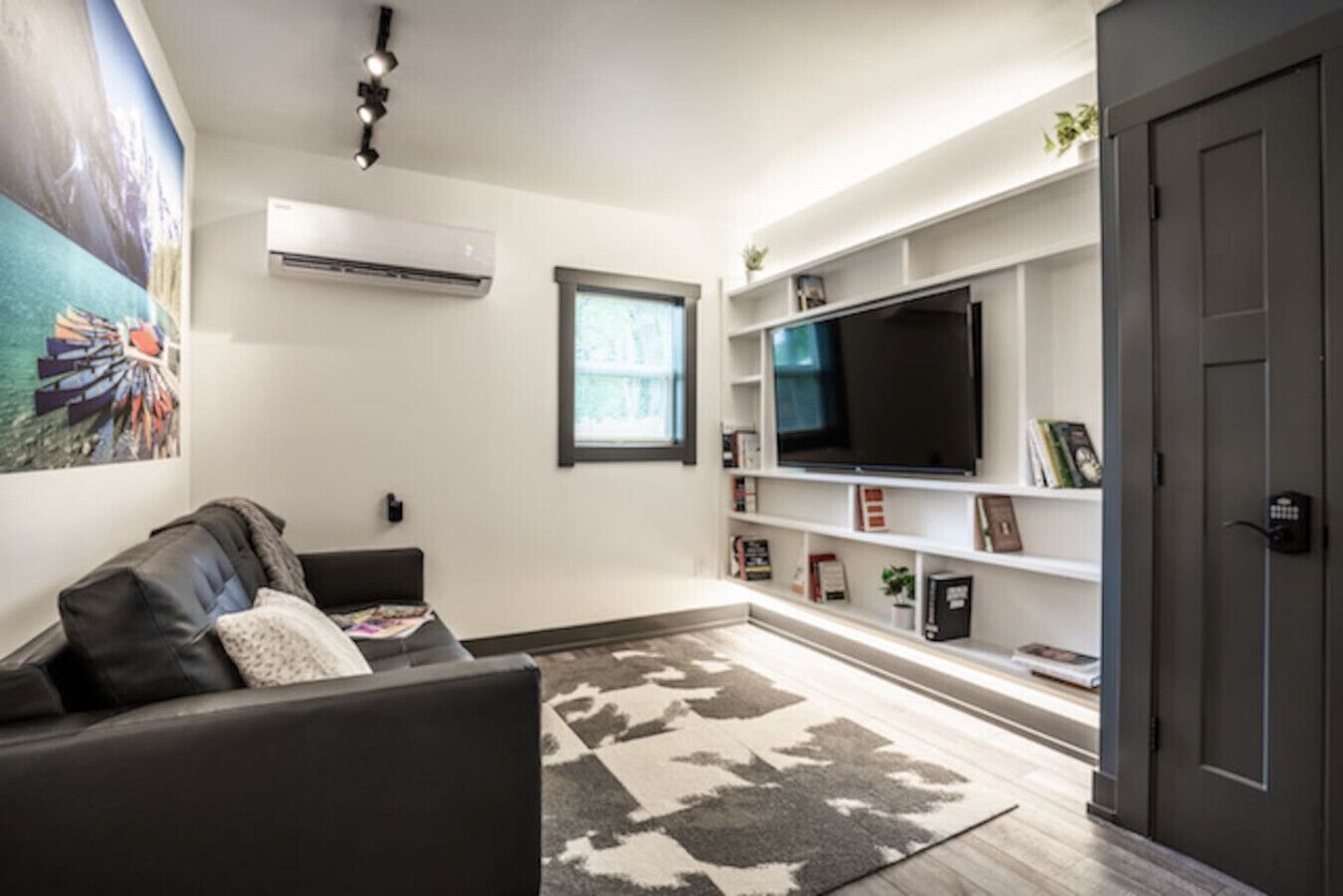 Un salon moderne comprenant un canapé, un téléviseur à écran plat, une bibliothèque et un appareil de climatisation.