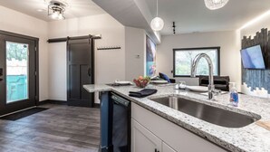 A modern kitchen with a large island, stainless steel sink, and pendant lighting. - Grand Park Modern Cubby 2BR/3BED/1BA/patio (Westfield)