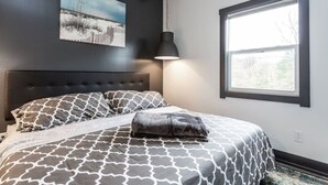 A bedroom with a large bed, a headboard, a hanging lamp, a window, and a painting on the wall. - Grand Park Modern Cubby 2BR/3BED/1BA/patio (Westfield)