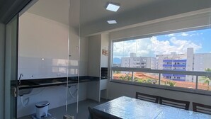 Une cuisine moderne avec une cloison en verre, une table à manger avec des chaises et une vue sur les immeubles à travers de grandes fenêtres.