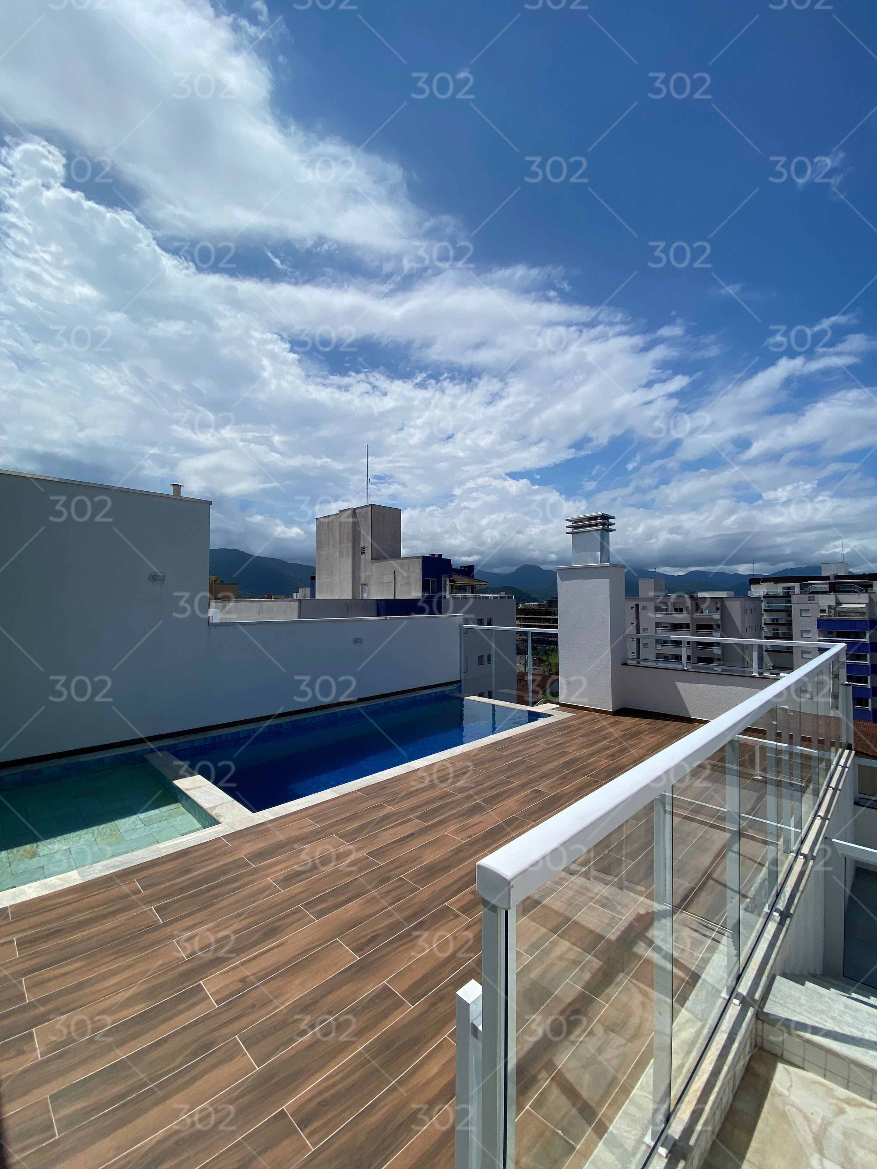 A rooftop pool area with a wooden deck and a glass railing.