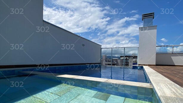 Une piscine sur le toit, avec une eau d’un bleu limpide, entourée d’un bâtiment blanc et surplombant un ciel dégagé.