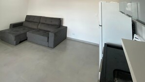 Un salon moderne avec un canapé d’angle, un réfrigérateur blanc et un éclairage encastré au plafond.